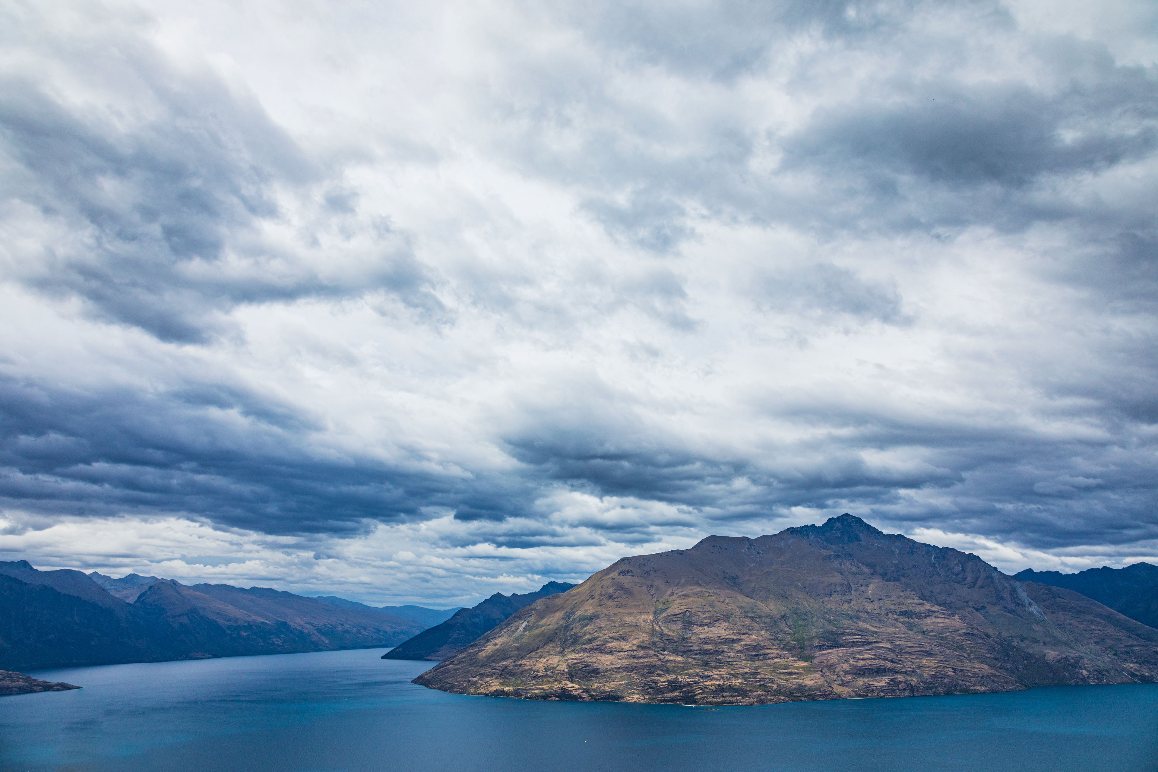 Vast blue lake and rugged mountains bathed in soft, diffused light under a dramatic, cloudy sky.