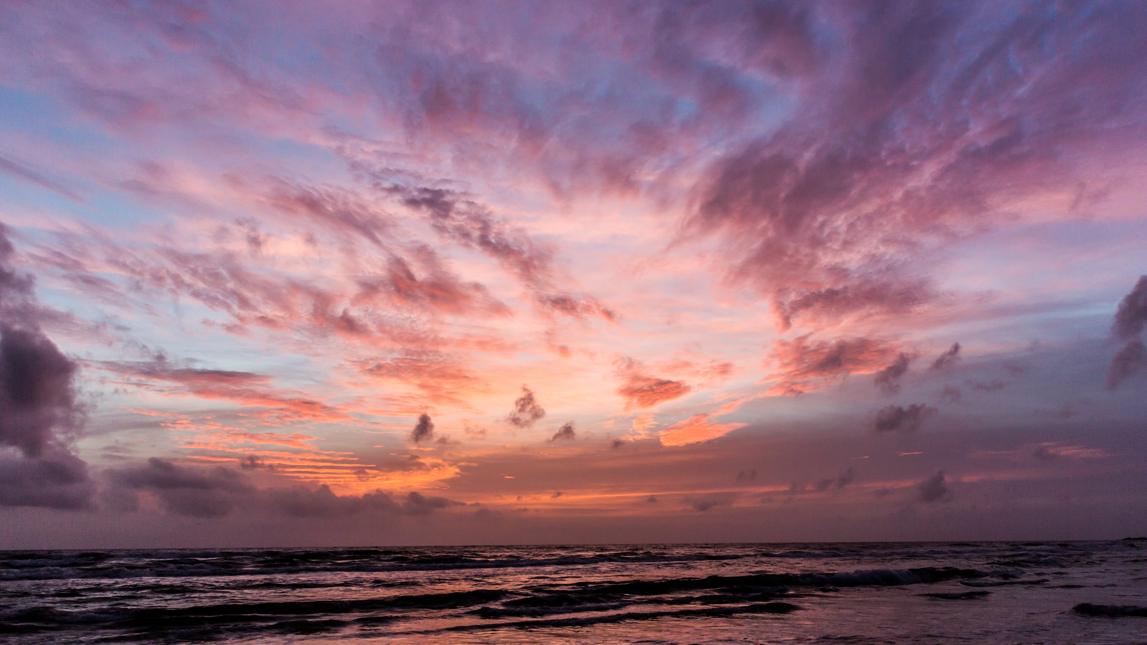 Mesmerizing sunset with a sky ablaze in pink, orange, and purple clouds, casting luminous reflections on the ocean waves.
